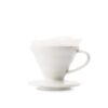 Handfilter auf Glashalter mit Kork. Tee wird aus einer Teekanne in die Tasse gekippt. Im Hintergrund: graue Couch und Pflanze.