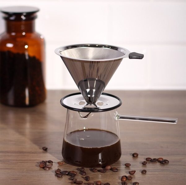 Handfilter auf Glaskanne mit Kaffee gefüllt. Davor Kaffeebohnen. Im Hintergrund ein verschwommenes Gefäß mit Kaffeebohnen.