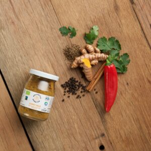 Bio Gewürz Curry Mild im Mehrwegglas, auf hölzernen Hintergrund mit Pfefferkörner, Zimtstange, Chilischote, Ingwar, Petersilie und Kümmel.