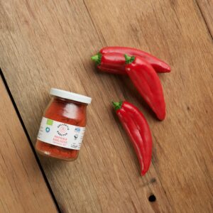 Bio Gewürz edelsüsse Paprika im Mehrwegglas, auf hölzernen Hintergrund mit drei roten Paprikaschoten.