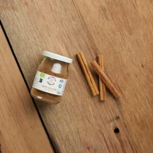 Bio Gewürz Zimt Ceylon im Mehrwegglas, auf hölzernen Hintergrund mit drei gehäuften Zimtstangen.