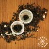 Fairtrade Bio Earl Grey verstreut auf hölzernem Hintergrund, mittig ein halbgefülltes Teeei offen.
