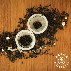 Fairtrade Bio Earl Grey verstreut auf hölzernem Hintergrund, mittig ein halbgefülltes Teeei offen.