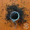 Fairtrade Bio Jasmin Tee verstreut auf hölzernem Hintergrund, mittig ein halbgefülltes Teeei offen.